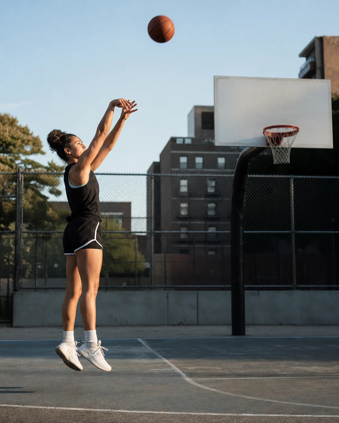 Female basketball player holding her follow-through on an outdoor city court