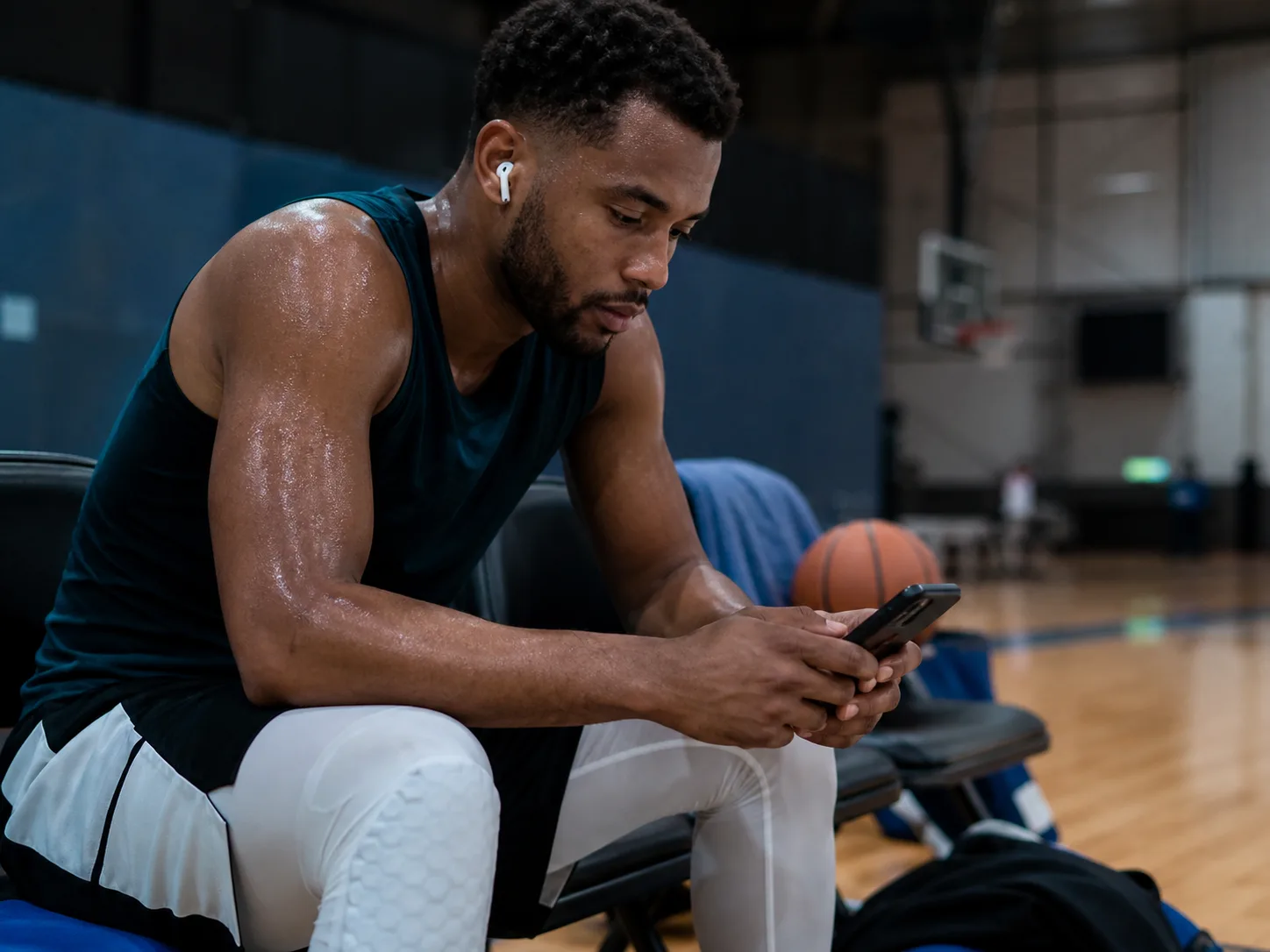 Basketball player reviewing training feedback on a smartphone from the sideline bench